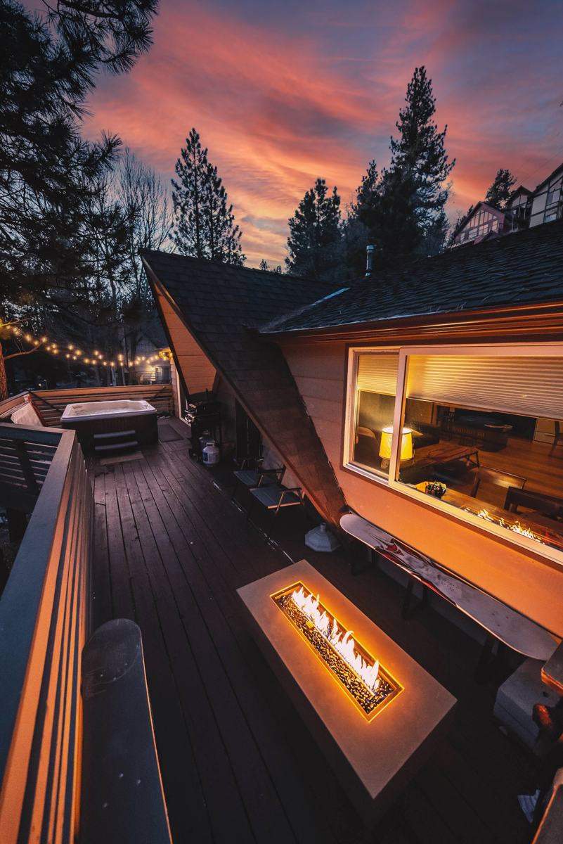 A cabin deck at dusk with a fire table and hot tub